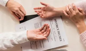 Dwie dłonie trzymają obrączki na tle dokumentu "DIVORCE DECREE". Zastanawiasz się, jak napisać papiery rozwodowe?