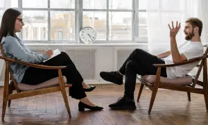 Kobieta w okularach notuje podczas sesji psychoterapii dynamicznej. Mężczyzna siedzi naprzeciwko, gestykulując.