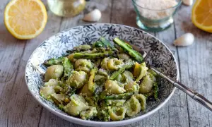 Un plat de pâtes aux asperges, garni de parmesan râpé, avec des citrons et de l'ail en arrière-plan.