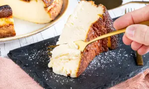 Ein Stück cremiger San Sebastian Cheesecake wird mit einer goldenen Gabel probiert.