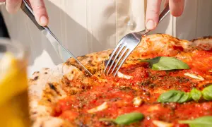Eine Pizza Marinara wird mit Messer und Gabel angeschnitten.
