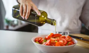 Une main verse de l'huile d'olive cuite sur une salade de tomates. Une touche saine pour contrôler le cholestérol.