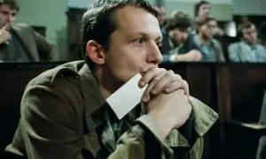 Młody mężczyzna zamyślony, trzymający kartkę przy ustach. Scena z filmu z nurtu **kino moralnego niepokoju**.