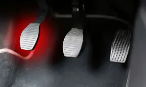 Pédales de voiture, dont celle de l'embrayage, avec une lumière rouge sur la gauche. Le **câble d'embrayage** est visible.