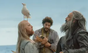 Trzech mężczyzn i mewa na głowie jednego z nich na tle nieba i morza.