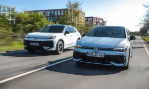 Två Volkswagen-bilar, en vit SUV och en ljusblå sedan, kör på en väg. Den vita bilen ser ut som en t-roc hybrid.