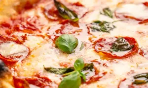 Nahaufnahme einer Pizza mit geschmolzenem Käse, roten Salami-Scheiben und frischem Basilikum. Verschiedene Salami-Sorten machen diese Pizza unwiderstehlich.