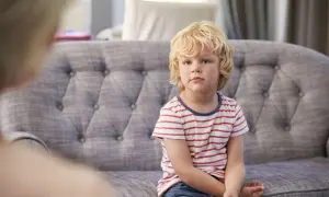 Chłopiec z blond włosami siedzi na kanapie w paski.