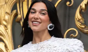 Uśmiechnięta Dua Lipa w białej kreacji, z dużymi kolczykami. Jej albańskie pochodzenie dodaje jej uroku.