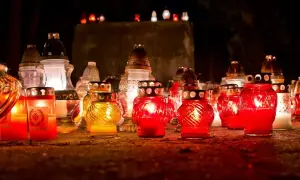 Wiele płonących zniczy na ciemnym tle, niektóre czerwone, inne żółte.