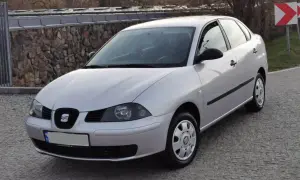 Srebrny Seat Cordoba zaparkowany na brukowanej drodze, z kamiennym murem w tle.