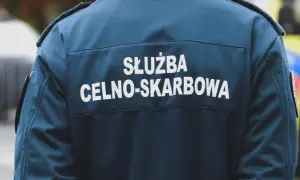 Celnik w granatowej kurtce z napisem "SŁUŻBA CELNO-SKARBOWA" stoi obok pojazdu.