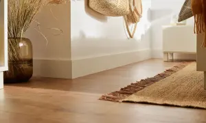 Elegancki montaż listwy przypodłogowej MDF podkreśla nowoczesne wnętrze. W wazonie suche trawy, obok pleciony kosz.