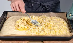 Mit einem Löffel werden Mandelblättchen auf den Teig für ein Blitzkuchen Rezept verteilt.