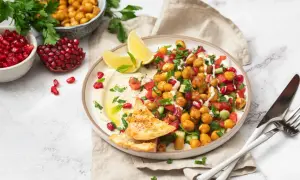 Bunter Kichererbsen Salat mit Granatapfelkernen, Tomaten, Gurken und Hummus, garniert mit Minze und serviert mit Pitabrot.