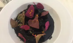 Un plat de ragout de seiche à l'encre noire, garni de pétales de fleurs séchées et d'une touche d'agrume.