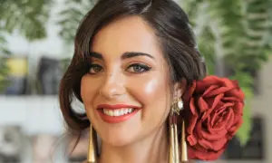Peinados para feria pelo corto: mujer sonriente con rosa roja en el cabello, pendientes dorados y maquillaje festivo.