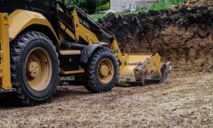 Koparka pracuje nad wyrównaniem działki ze spadkiem, przesuwając ziemię.