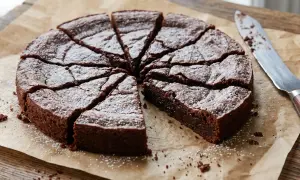 En saftig kladdkaka, pudrad med florsocker, skuren i bitar på bakplåtspapper. En kniv ligger bredvid, redo att skära fler bitar av denna härliga kladdkaka.