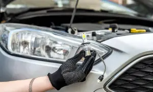 Ręka w rękawiczce trzyma nową żarówkę LED do wymiany przedniego reflektora w Peugeot 207.