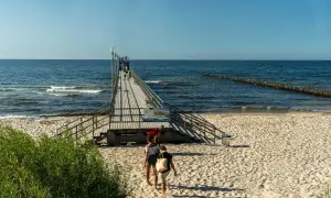 Sianożęty atrakcje: drewniane molo na plaży, ludzie spacerują, morze i niebo.