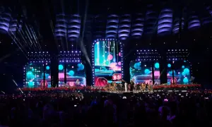 Wydarzenia na Stadionie Narodowym: scena z neonowymi samochodami i tańczącymi artystami, oświetlona przez reflektory. Tłum widzów wpatrzony w widowisko.