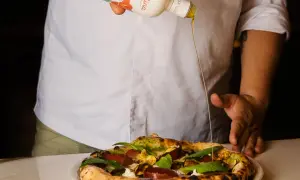 Un cuoco versa l'olio Coratina migliore su una pizza gourmet. L'olio extra vergine d'oliva esalta i sapori.