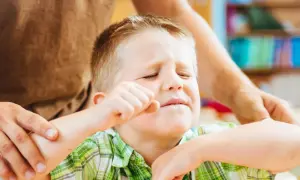 Chłopiec zamyka oczy, zaciska pięść, a dorosły trzyma go za ramię. Szukamy odpowiedzi, jak leczyć ADHD, by pomóc dzieciom.