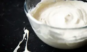 Schlagrahm in einer Glasschüssel, bereit für ein Dessert. Ein Klecks Sahne ist daneben auf der dunklen Arbeitsfläche zu sehen.