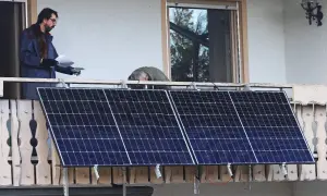 Dos hombres instalan placas solares en una terraza. Uno revisa un papel mientras el otro se inclina sobre los paneles.