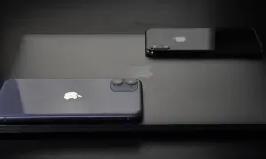Dwa iPhone'y, w tym jeden fioletowy, leżą na czarnym laptopie. Zastanawiasz się, jak wyłączyć iPhone'a 11?