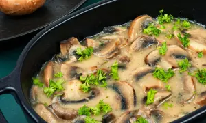 Duszone pieczarki w sosie, udekorowane natką pietruszki, w czarnej misie.