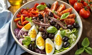 Salade de riz niçoise colorée avec œufs durs, tomates, poivrons, olives, anchois et basilic frais. Un délice méditerranéen.