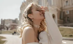 Uśmiechnięta blondynka w perłowej biżuterii, z wpiętymi we włosy prawdziwymi perłami, cieszy się słońcem.