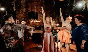 Oczepiny co to? Zabawa weselna w pełni! Panie w sukniach i panowie bawią się przy neonowym napisie "Let's Dance!".