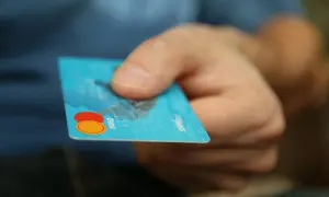 Dłoń trzyma niebieską kartę debetową z logo Mastercard.