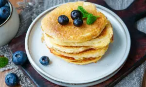 Ein Stapel fluffiger **Protein Pfannkuchen** mit Blaubeeren und Minze, bestäubt mit Puderzucker.