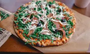 Pizza z rukolą, szynką parmeńską i oliwkami, posypana obficie startym parmezanem do pizzy.