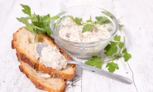 Une cuillère dépose des rillettes de maquereau sur une tranche de pain grillé, à côté d'un bol rempli de cette délicieuse préparation.