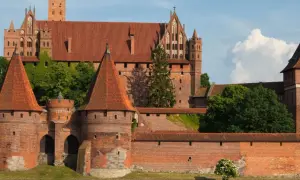Potężny zamek w Malborku, wpisany na listę UNESCO w Polsce, z czerwonymi dachami i zielenią.