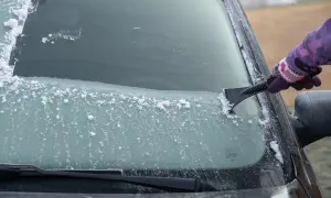Ręka w rękawiczce zeskrobuje szron na szybie samochodu. Zima daje się we znaki, ale widok czystej szyby jest nagrodą.