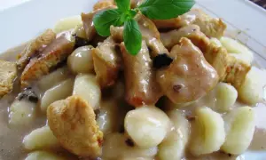 Pyszne gnocchi z kurczakiem w sosie śmietanowym, udekorowane listkiem bazylii. Danie wygląda apetycznie i sycąco.
