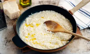 Krämig parmesanrisotto i en panna, med en träsked som rör om. Ingredienser som parmesanost och olivolja syns i bakgrunden.