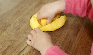 Kleine Hände erkunden eine aufgeschnittene Mango. Ab wann darf ein Baby Mango essen?