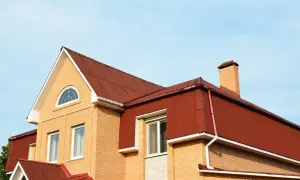Jasny dom z cegły, czerwony dach i okna mansardowe.