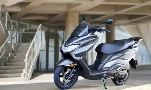 Szary skuter Suzuki Burgman, znany jako jeden z najbardziej bezawaryjnych skuterów, zaparkowany przed nowoczesnym budynkiem z betonowymi schodami.