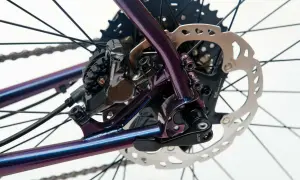 Błyszcząca, fioletowa rama roweru z widoczną sztywną osią w rowerze, hamulcem tarczowym Shimano i kasetą.