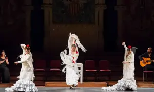 Mujeres en un apasionado baile flamenco, con trajes blancos y volantes, acompañadas por un guitarrista.