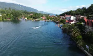 Ein Boot rast über den See, während man die Hügel und Häuser von Sumatra beim Backpacking genießt.