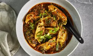 En skål med ångande dumplings i en kryddig sås, toppad med salladslök och sesamfrön. Perfekt för snabba vegetariska recept.